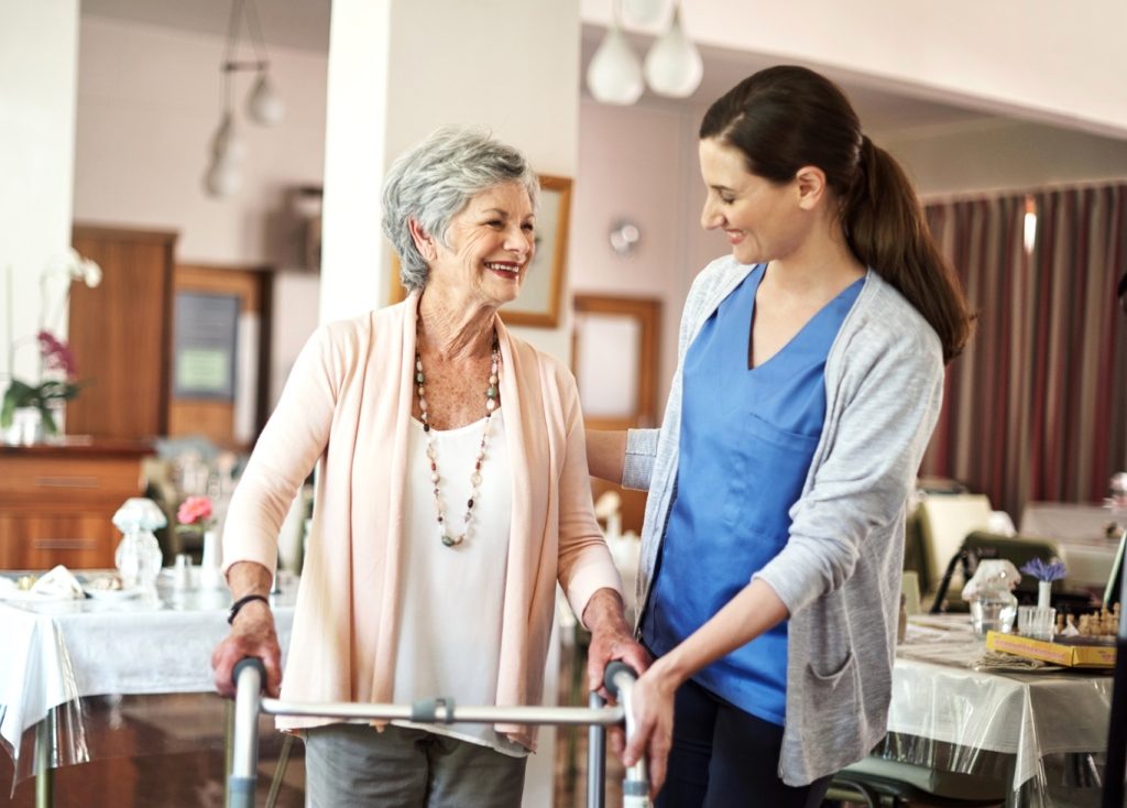 Residential care nurse helping elderly woman with walking frame